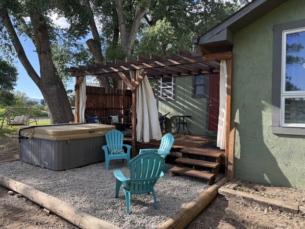 A patio area with a hot tub, two Adirondack chairs, and a wooden pergola.