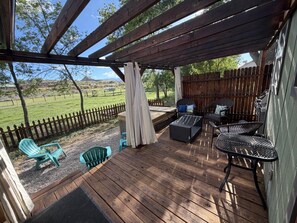A covered outdoor patio with wooden flooring, green Adirondack chairs, a black metal table, and a wooden fence in the background. - Peaceful Farmhouse - Hot Tub - Office (Silt)