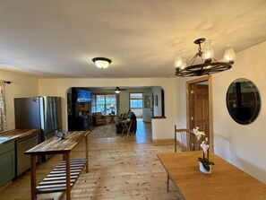 A spacious living area with a wooden dining table, a kitchen with a refrigerator, and a ceiling fan.