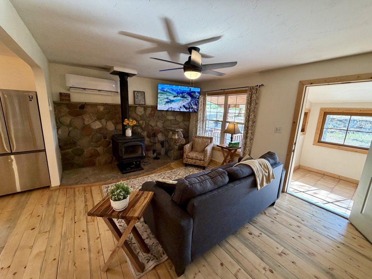 A living room with a stone fireplace, a sofa, a television, and a ceiling fan.