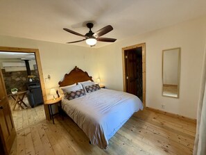 A bedroom with a bed, a ceiling fan, a nightstand, and a stone fireplace.
