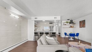 Ein modernes Wohnzimmer mit einer Couch, einem Essbereich mit blauen Stühlen und einer Küche im Hintergrund.