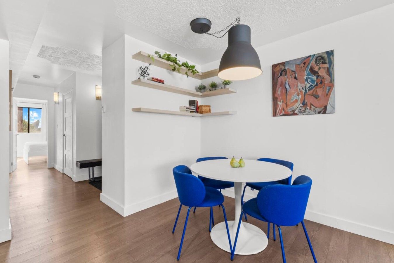 A modern dining area with a round table and blue chairs, white walls, and a ceiling light fixture.