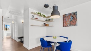 Ein moderner Essbereich mit einem runden Tisch und blauen Stühlen, weißen Wänden und einer Deckenleuchte.