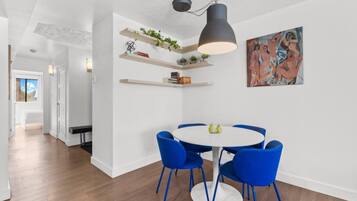 A modern dining area with a round table and blue chairs, white walls, and a ceiling light fixture.