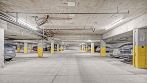 Eine mehrgeschossige Tiefgarage mit Betonpfeilern, nummerierten Parkplätzen und sichtbaren Konstruktionselementen wie Rohren und Leitungen.