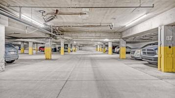 A multi-level underground parking garage with concrete pillars, numbered parking spaces, and visible structural elements like pipes and ducts.