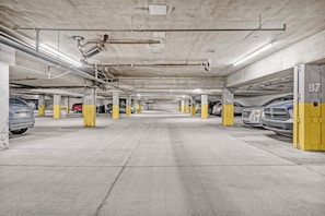 A multi-level underground parking garage with concrete pillars, numbered parking spaces, and visible structural elements like pipes and ducts. - 2BR City Retreat | Stampede, BMO & Free Parking (Calgary)