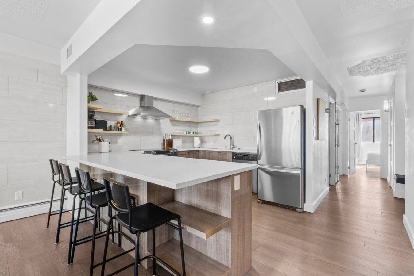 A modern kitchen with a large island, bar stools, stainless steel appliances, and a wooden floor.