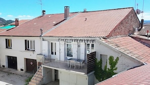 A two-story building with a red-tiled roof, a balcony with a metal railing, and a staircase leading to the entrance. - Appartement cosy et confortable. Chez Lyne. (Laragne-Montéglin)