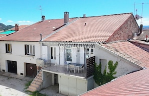 A two-story building with a red-tiled roof, a balcony with a metal railing, and a staircase leading to the entrance. - Appartement cosy et confortable. Chez Lyne. (Laragne-Montéglin)