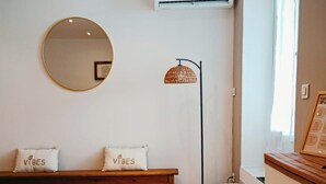 A room with a round mirror, a bench with two pillows, a floor lamp, and a staircase.