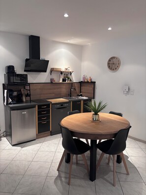 Una cocina moderna equipada con microondas, tostadora y lavavajillas, una mesa de comedor de madera con sillas y un reloj en la pared.