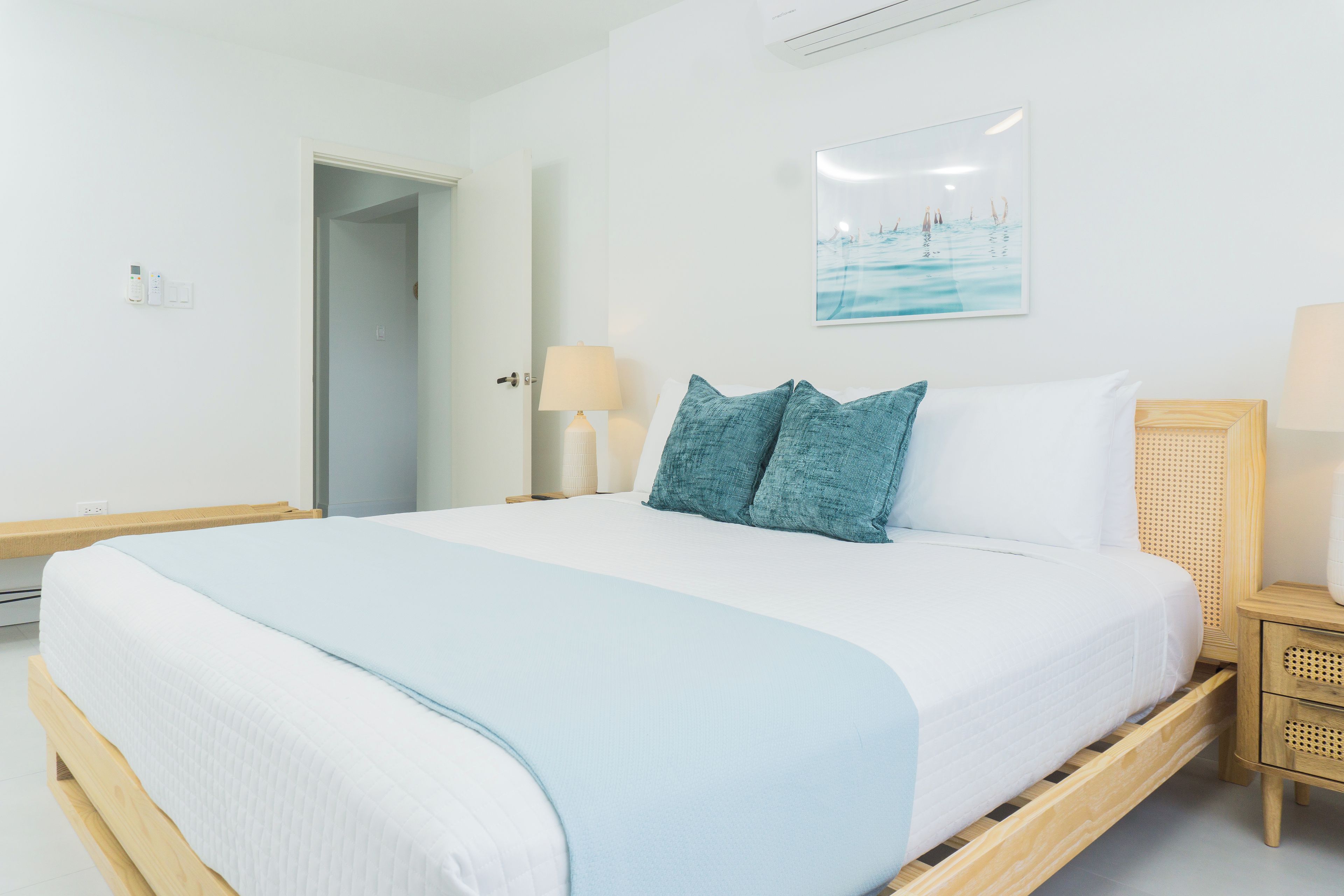 Una habitación de hotel con cama, mesitas de noche, una lámpara y un cuadro en la pared.