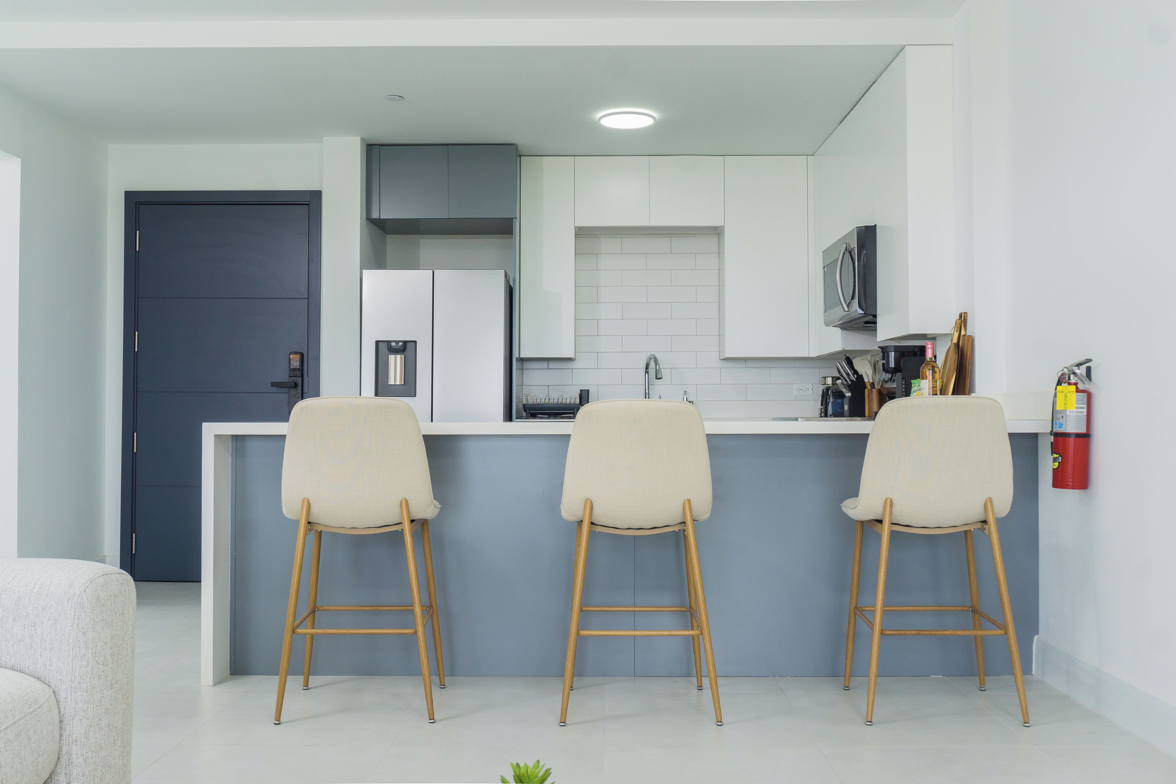 Une cuisine moderne avec un coin bar, des meubles blancs et une porte grise.