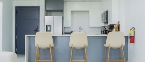 A modern kitchen with a bar area, white cabinets, and a grey door.