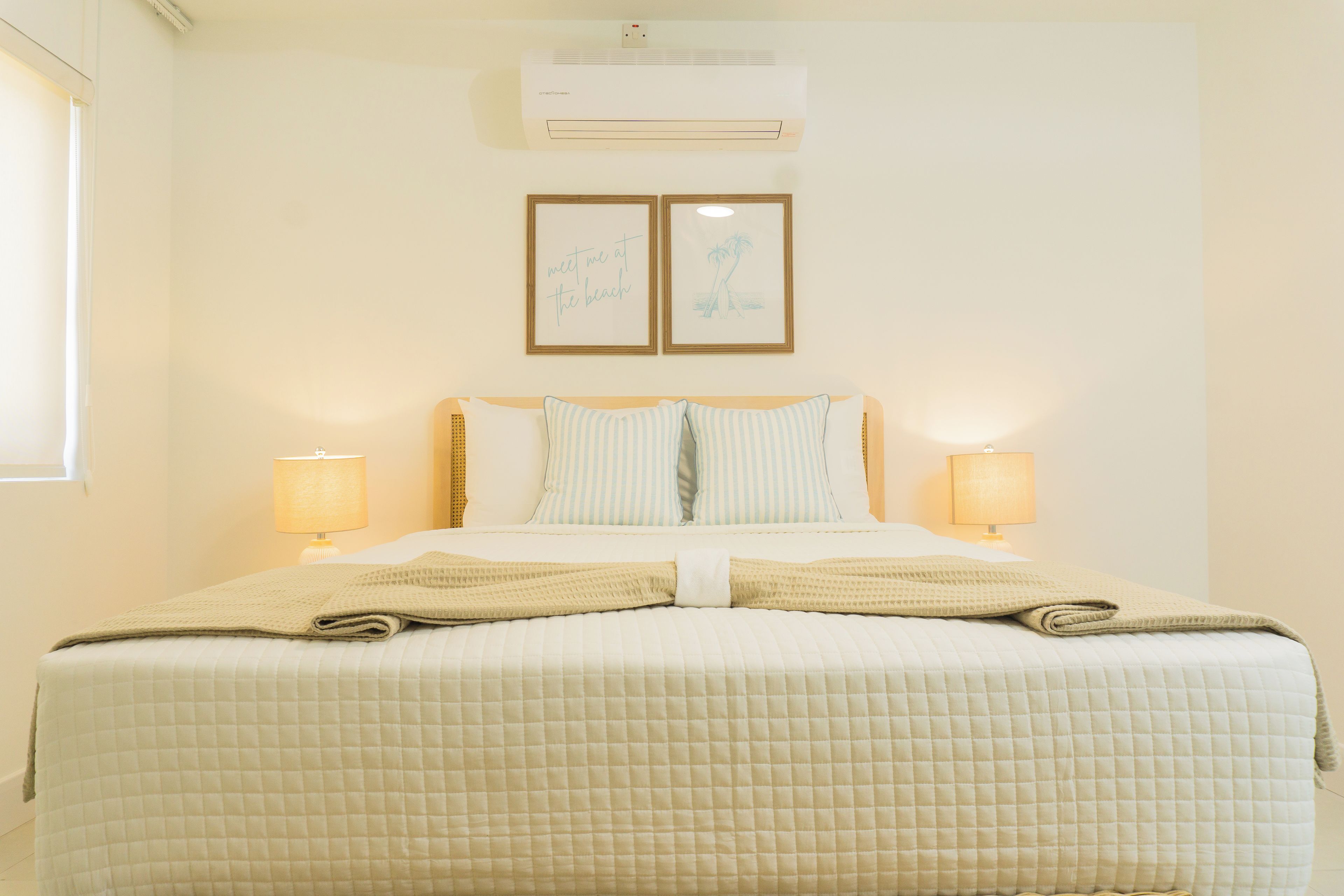 Une chambre d’hôtel avec un lit, deux lampes de chevet, un climatiseur et deux tableaux encadrés au mur.