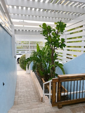A covered outdoor pathway with a wooden railing, surrounded by greenery and a white fence. - Direct Oceanfront Retreat with Ocean-to-River Views  Sleeps 8 (Cocoa Beach)