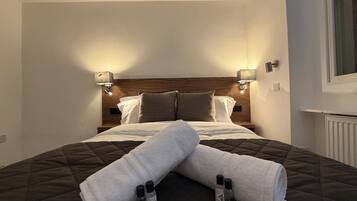 Un lit bien fait, avec une tête de lit matelassée, deux lampes de chevet et une fenêtre sur le côté droit.