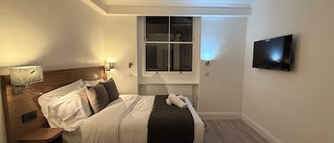 A hotel room with a bed, a nightstand, a lamp, a window, and a television.