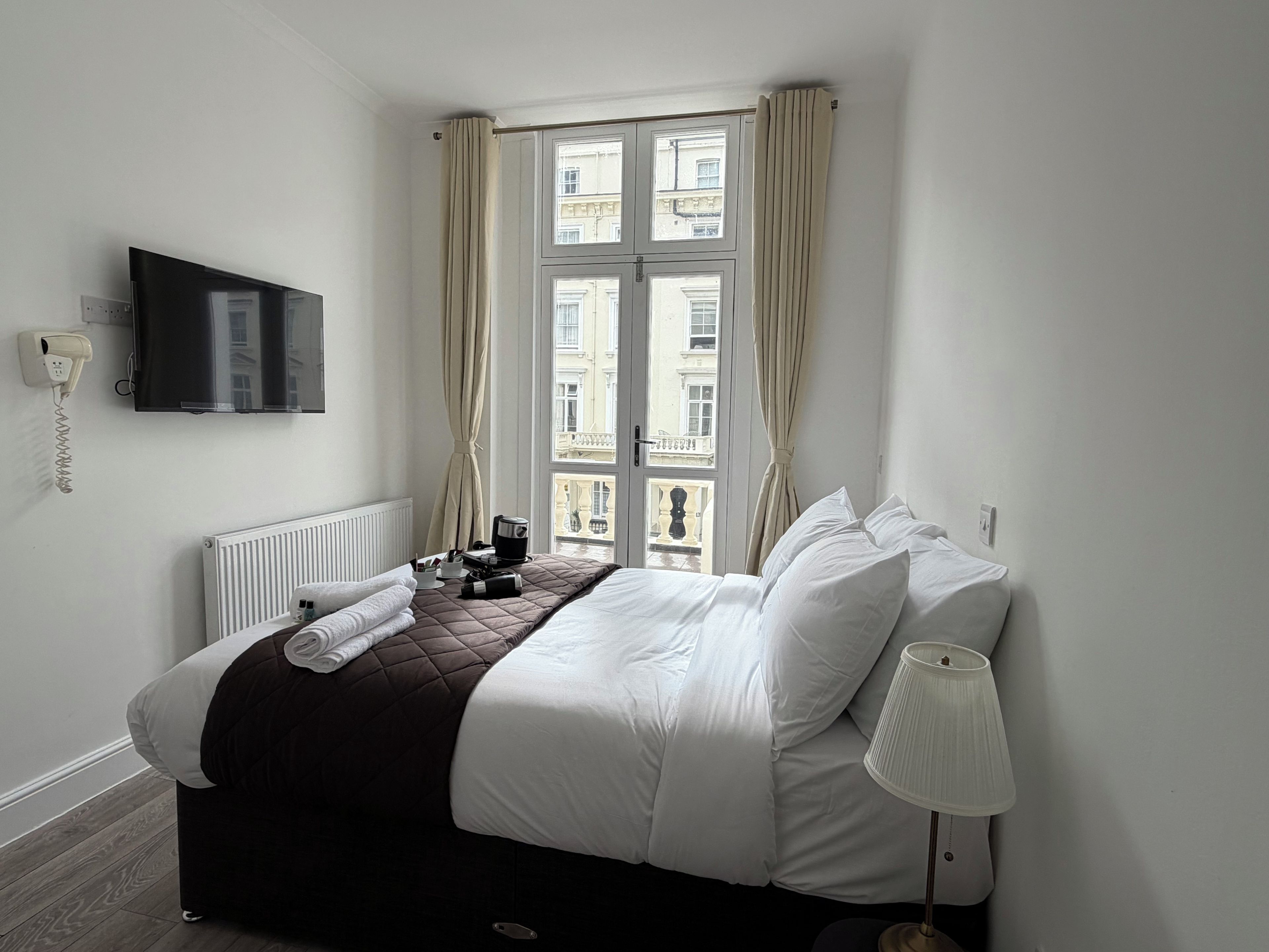 Een hotelkamer met een bed, een aan de muur bevestigde televisie, een raam met gordijnen en een bedlampje.