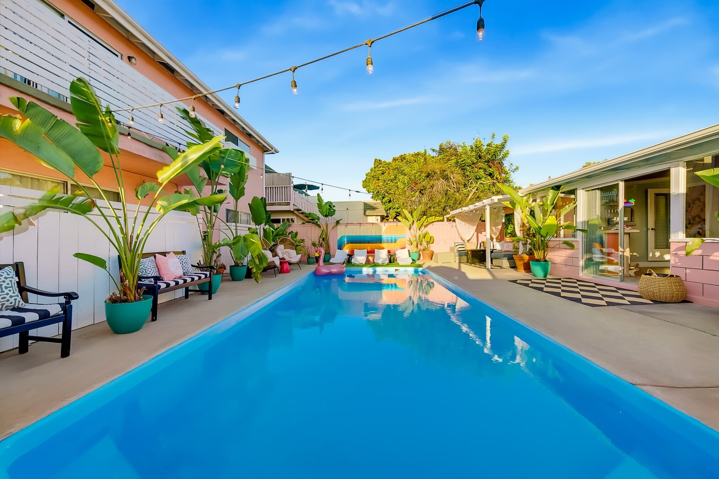 A swimming pool with a clear blue water surface, surrounded by potted plants and outdoor furniture.