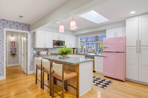 A modern kitchen with white cabinets, a pink refrigerator, and a central island with bar stools. - Good Vibes & Poolside Nights | San Diego (San Diego)