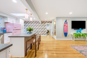 Eine moderne Küche mit einem rosa Kühlschrank, Holzbarhocker und einem Essbereich mit Holzboden.
