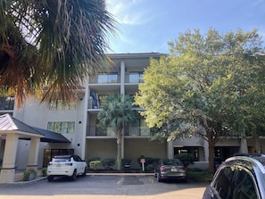 A multi-story building with a parking area in front. - Village House 204 | Relax & Walk to the Beach (Hilton Head Island)