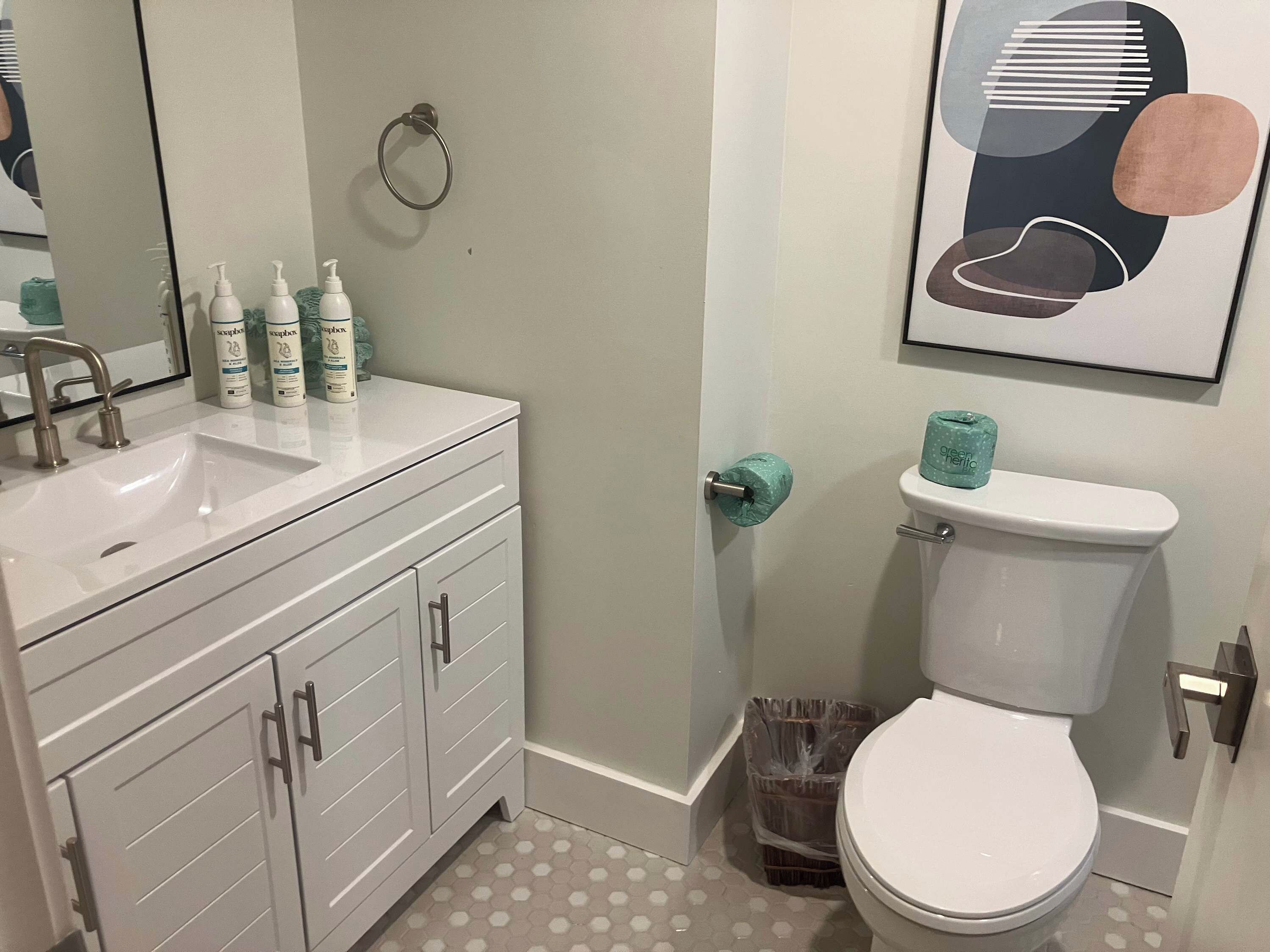 A bathroom with a white sink, toiletries, a toilet, and a trash bin.