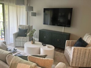 A modern living room with a sofa, armchairs, a coffee table, a TV, and a cabinet. - Village House 204 | Relax & Walk to the Beach (Hilton Head Island)
