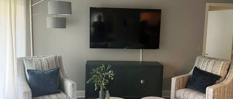 A modern living room with two patterned armchairs, a round coffee table, a television mounted on the wall, and a dark-colored cabinet.