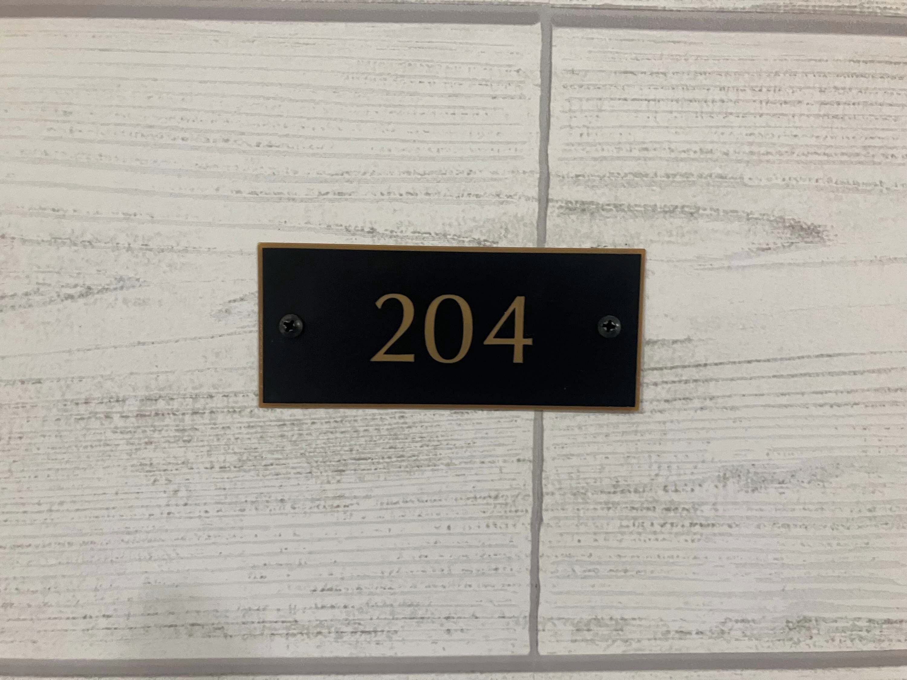 A black rectangular sign with the number 204, mounted on a white textured wall.