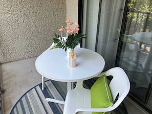 Una mesa redonda pequeña con un florero de flores, una silla con cojín verde y una pared texturizada al fondo.
