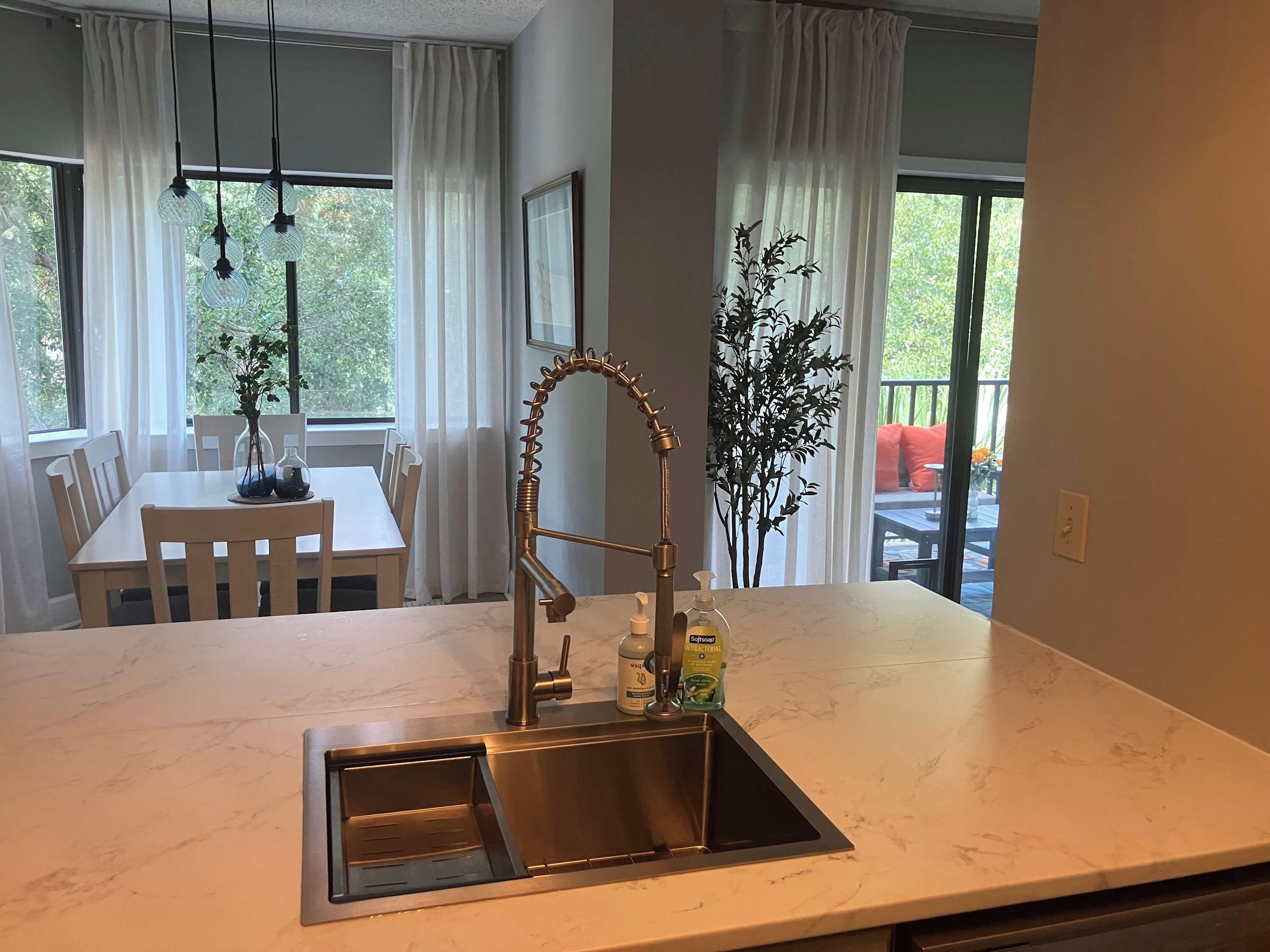 Une cuisine dotée d’un évier en acier inoxydable, d’un robinet moderne et d’un plan de travail en marbre. On y trouve une table à manger avec des chaises et un vase rempli de fleurs.