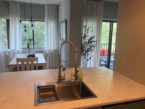 A kitchen with a stainless steel sink, a modern faucet, and a marble countertop. There is a dining table with chairs and a vase with flowers. - Village House 204 | Relax & Walk to the Beach (Hilton Head Island)