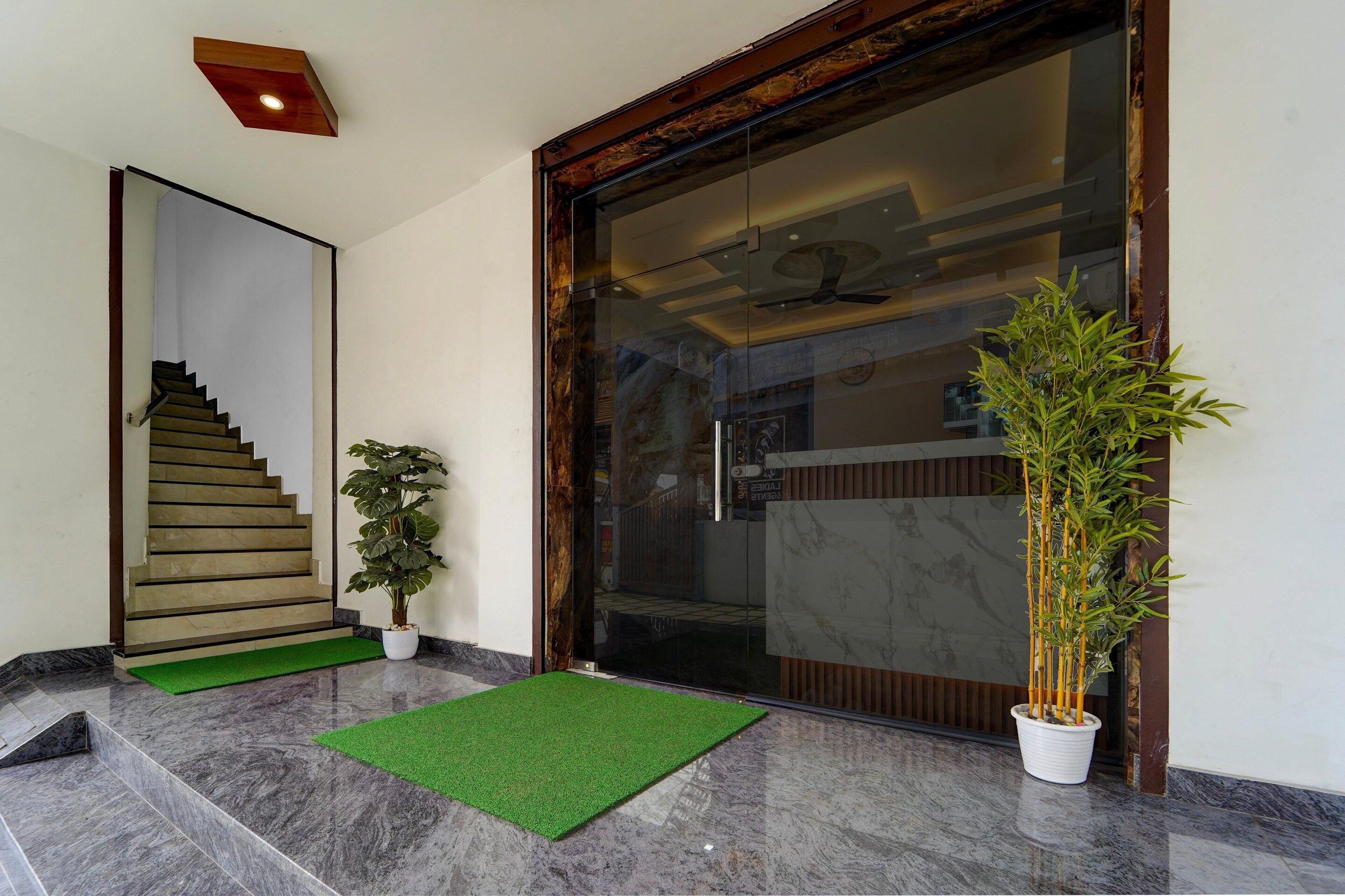 A modern entrance with a glass door, a wooden staircase, and a green mat.
