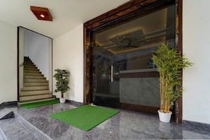 A modern entrance with a glass door, a wooden staircase, and a green mat. - Deluxe Apsara Tourist Homes (Adoor)