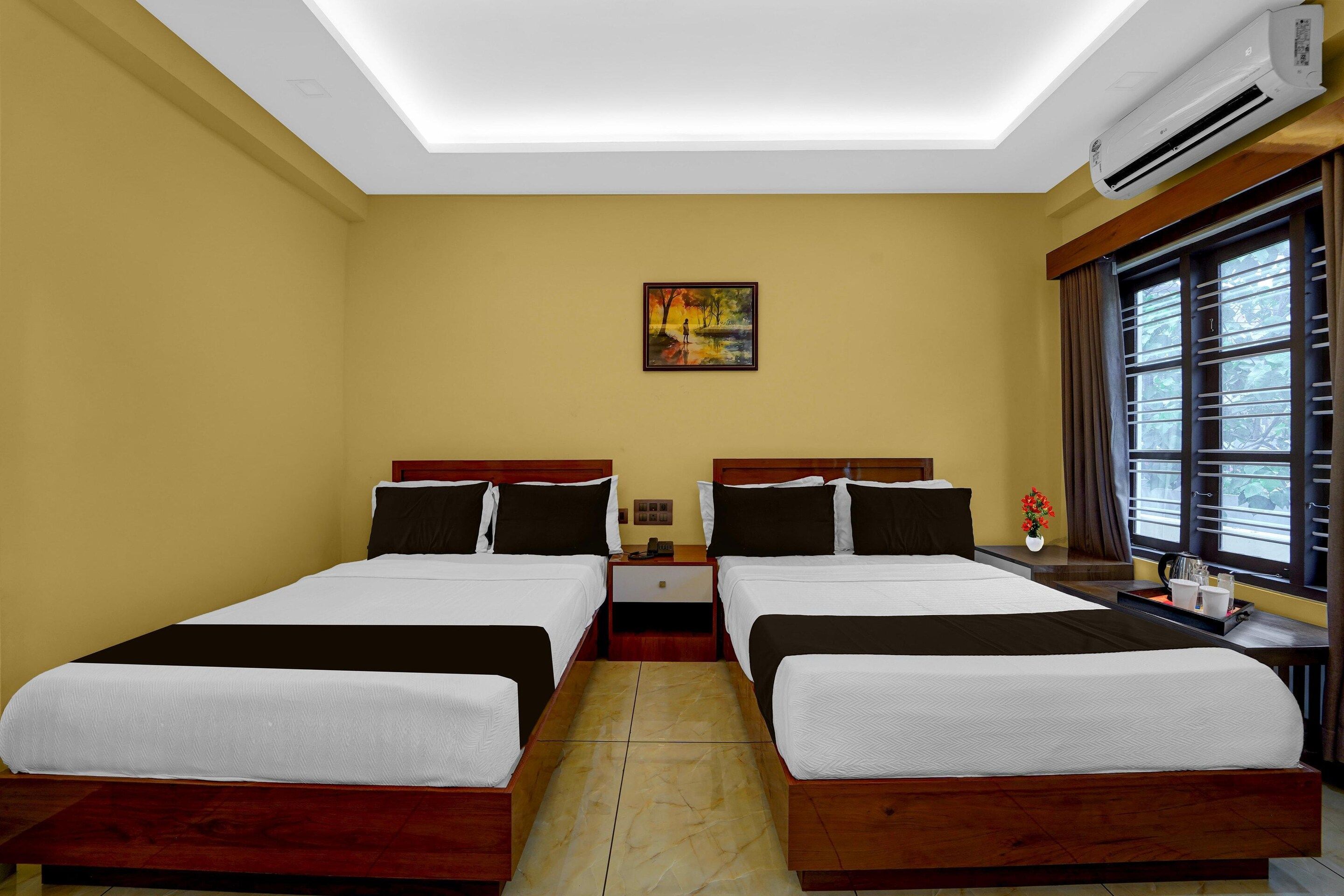 A hotel room with two beds, a painting on the wall, and a window with blinds.