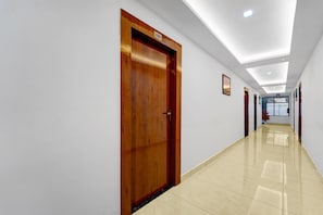 Un pasillo con puerta de madera, paredes blancas y suelo de baldosas.