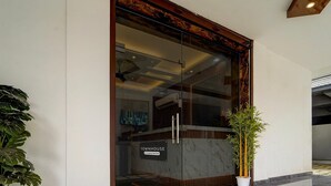 En moderne bygningseingang med en glasdør, et receptionsskrank og en potteplante.