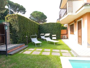 Ein Innenhof mit Schwimmbad, drei Liegestühlen, einer Hecke und einem Gebäude mit Balkon.