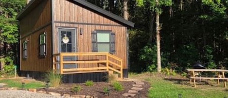 Ein kleines Holzhaus mit Veranda und Picknicktisch inmitten eines bewaldeten Geländes.