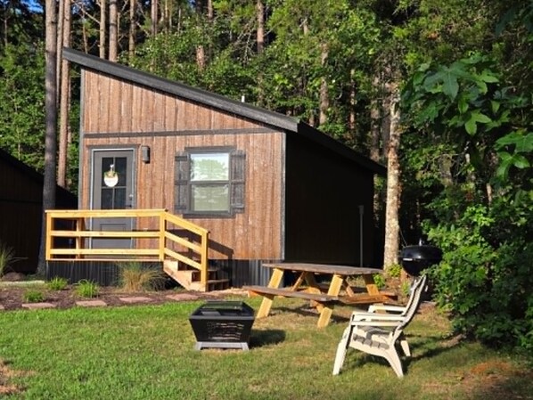 Een houten chalet met een veranda, een barbecue en een picknicktafel.