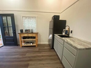 A compact kitchen with a built-in oven, a refrigerator, and a wooden shelf with cookware. - Hummingbird is a Cozy & Quaint 1 bedroom Cabin bordering Ozark National Forest (Dover)
