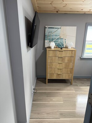 Una habitació amb un armari de fusta, televisió penjada a la paret i un quadre d'un veler.