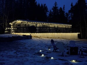A cabin with a deck, outdoor seating, and snow on the ground.