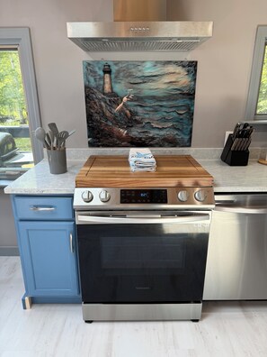 A kitchen with a stainless steel range hood, a Samsung oven, a wooden countertop, and a painting of a lighthouse.