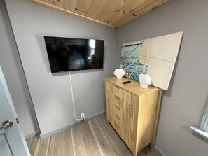 A room with a flat-screen TV mounted on the wall, a wooden cabinet with two decorative vases, and a painting above the cabinet.