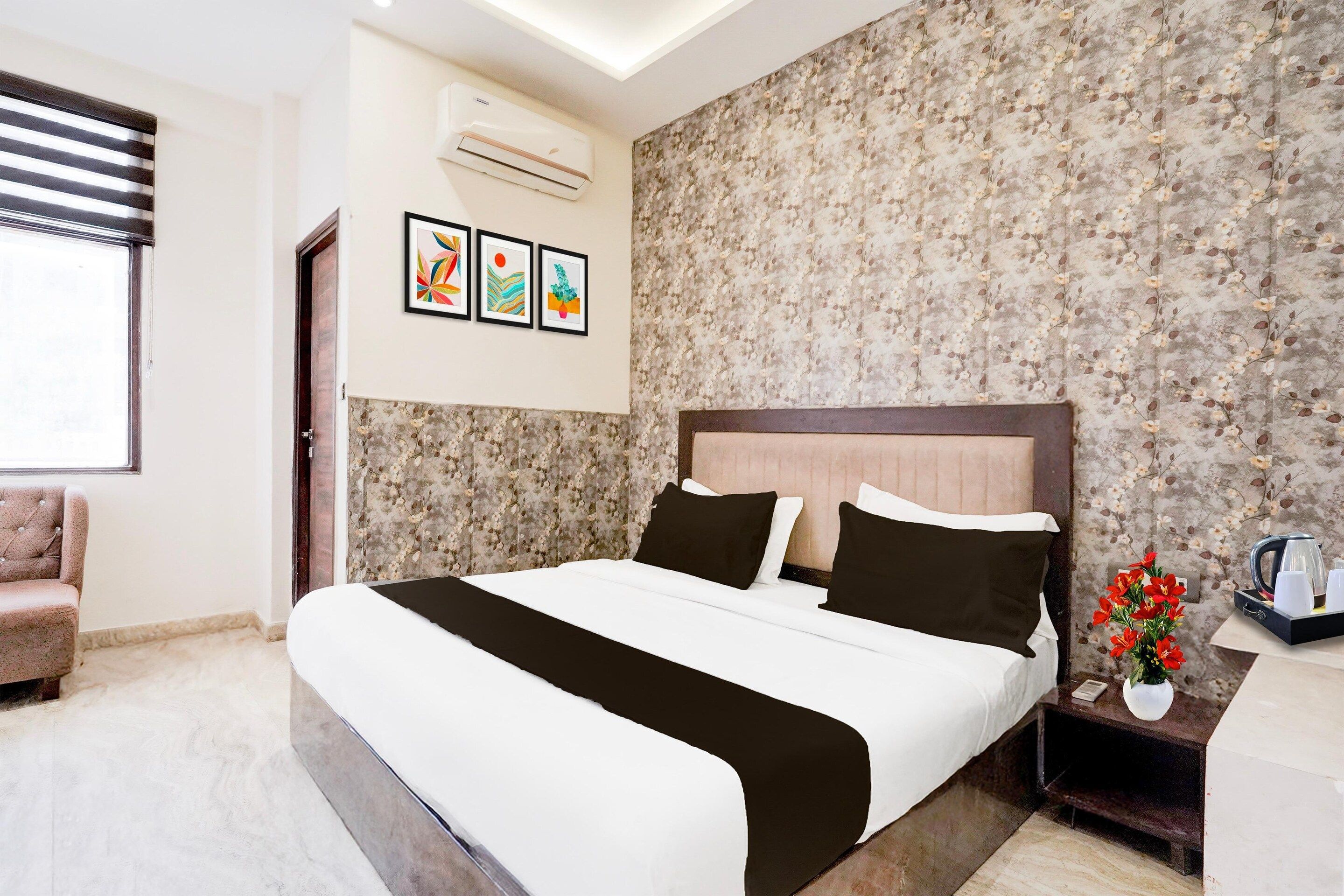 A hotel room with a bed, a chair, a nightstand, a coffee maker, and a floral wallpaper.